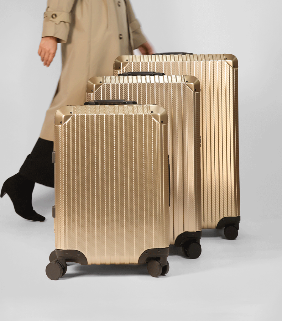 Set of gold suitcases with a person wearing a trench coat in the background